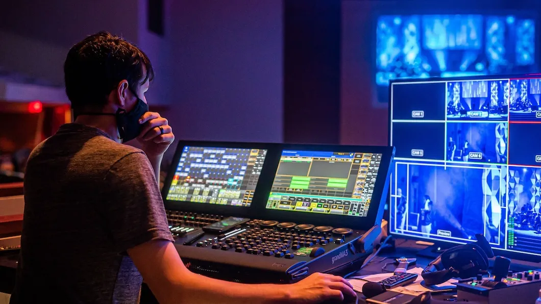 A stage manager looks at a lighting board and monitor.