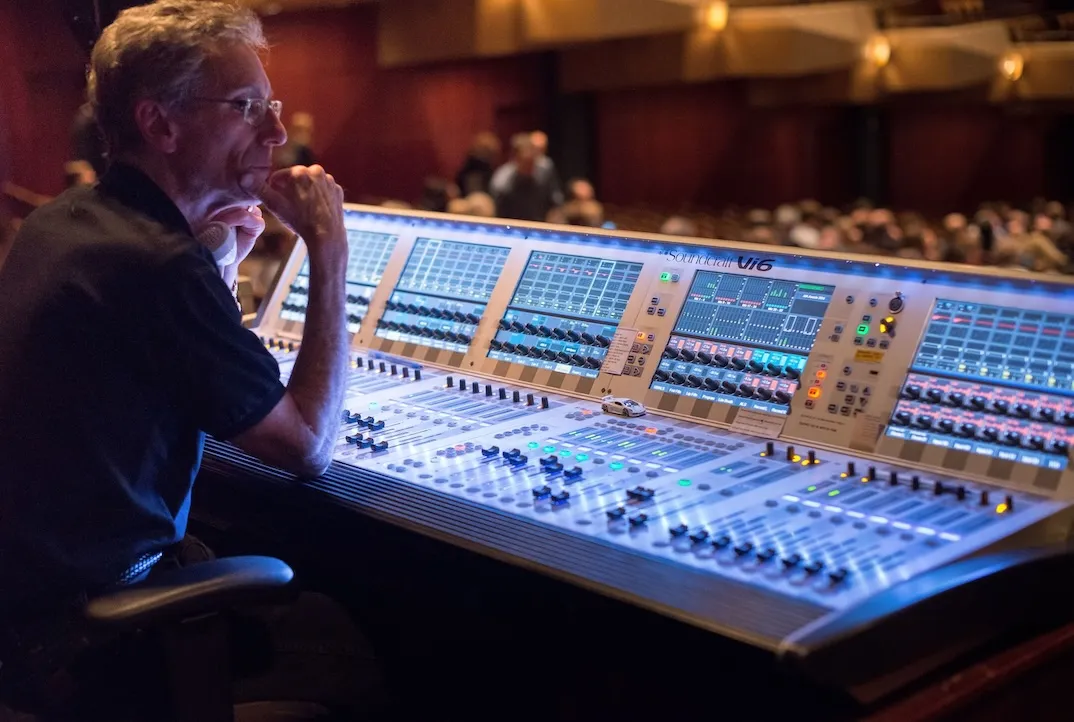 a sound designer looks at the stage in front of a large sound console.