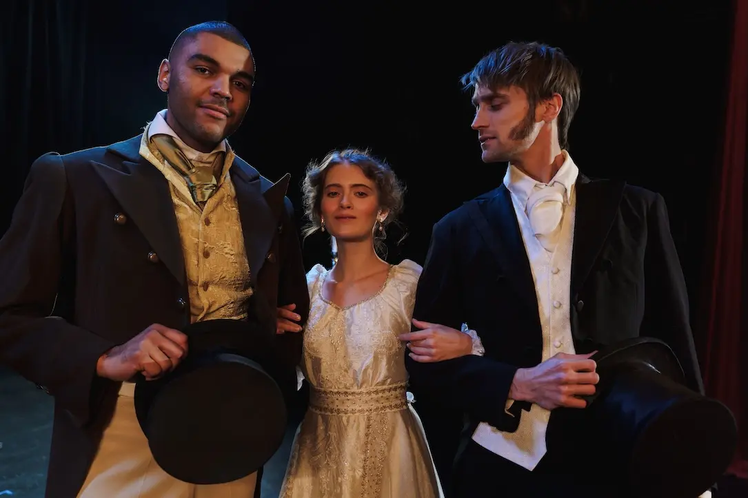 an actress locks hands with two actors in matching costumes.