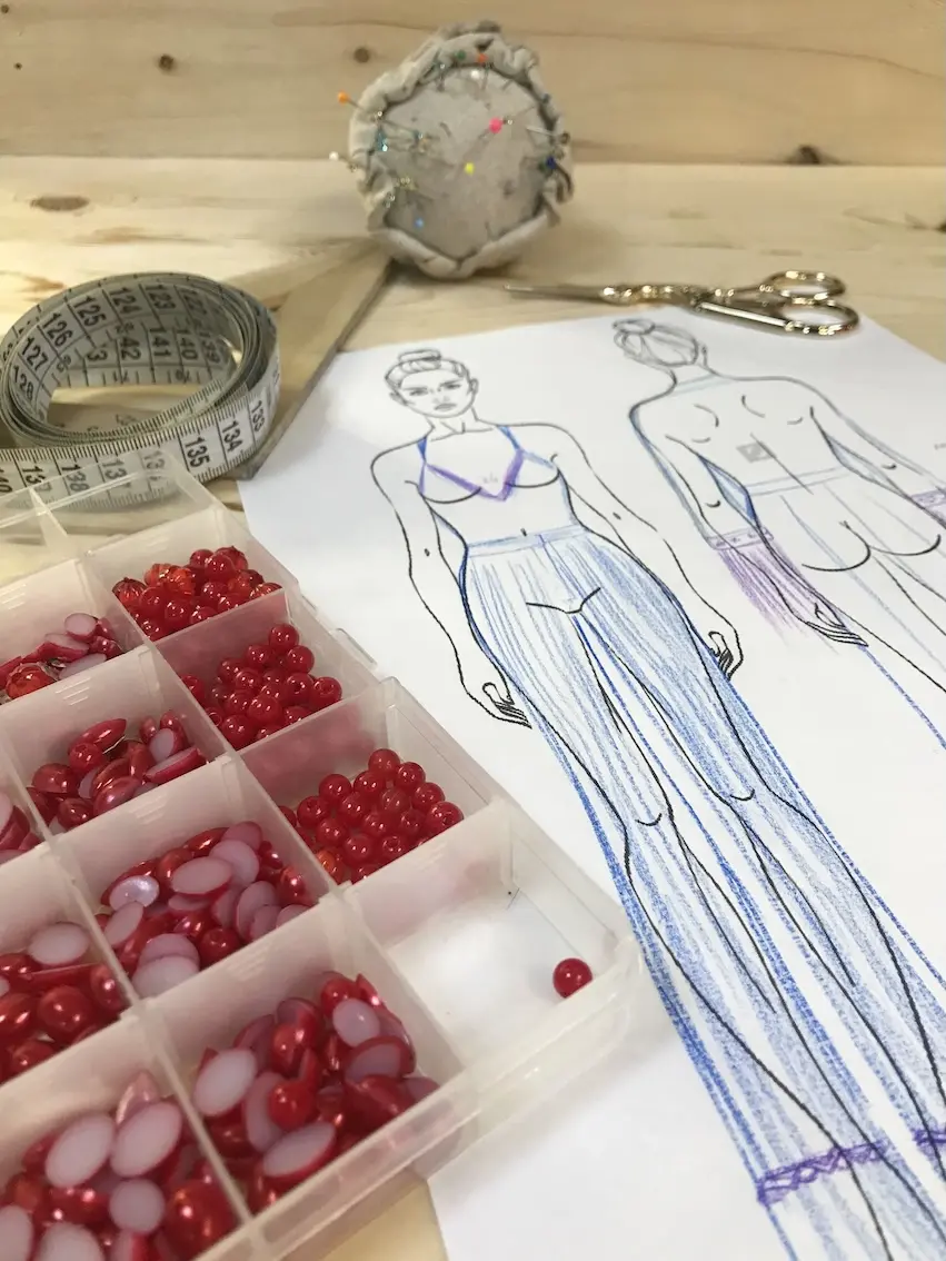a costume sketch laying ona. table next to beads and fabric samples.