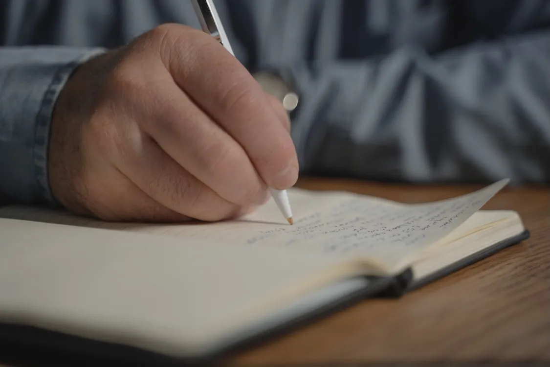 a hand holding a pen writes on a notebook